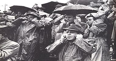 Pic of a group of people wearing raincoats and holding umbrellas with their fingers in their ears.