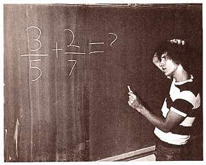 boy in classroom looking at a math problem on the chalkboad and scratching his head.